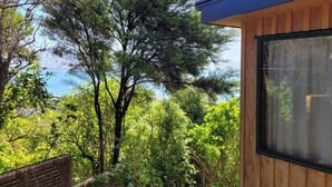 A wooden building with a large window, surrounded by dense greenery and trees. - Tata Beach Heights - Spectacular Ocean and Bush Views (Tata Beach)