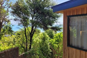 A wooden building with a large window, surrounded by dense greenery and trees. - Tata Beach Heights - Spectacular Ocean and Bush Views (Tata Beach)