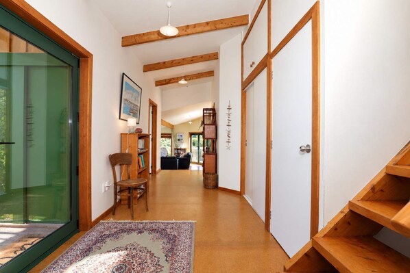 A hallway with wooden beams, a chair, a bookshelf, and a patterned rug.