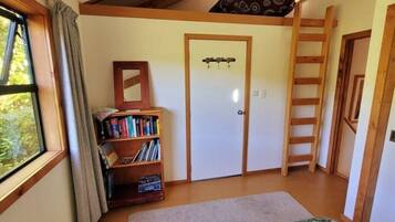 Una habitación con cama tipo altillo, una escalera de madera, una estantería y una puerta con espejo.