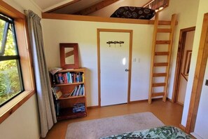 A room with a loft bed, a wooden ladder, a bookshelf, and a door with a mirror. - Tata Beach Heights - Spectacular Ocean and Bush Views (Tata Beach)