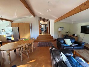 A spacious living area with a dining table, a sofa, and a kitchen area with appliances. - Tata Beach Heights - Spectacular Ocean and Bush Views (Tata Beach)