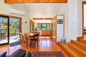 A modern kitchen with a dining area, wooden flooring, and a view of greenery outside. - Tata Beach Heights - Spectacular Ocean and Bush Views (Tata Beach)