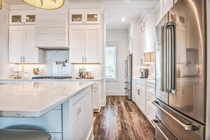 Una cocina moderna con armarios blancos, una isla de mármol, electrodomésticos de acero inoxidable y suelo de madera.