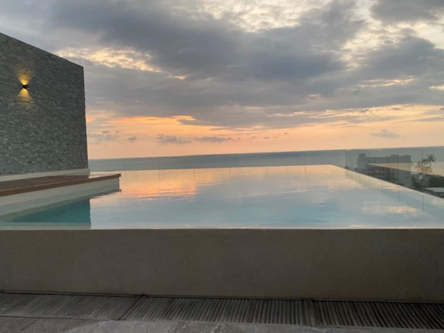 Una piscina infinita rectangular con una vista despejada del horizonte, una pared texturizada en un lateral y un cielo sereno.