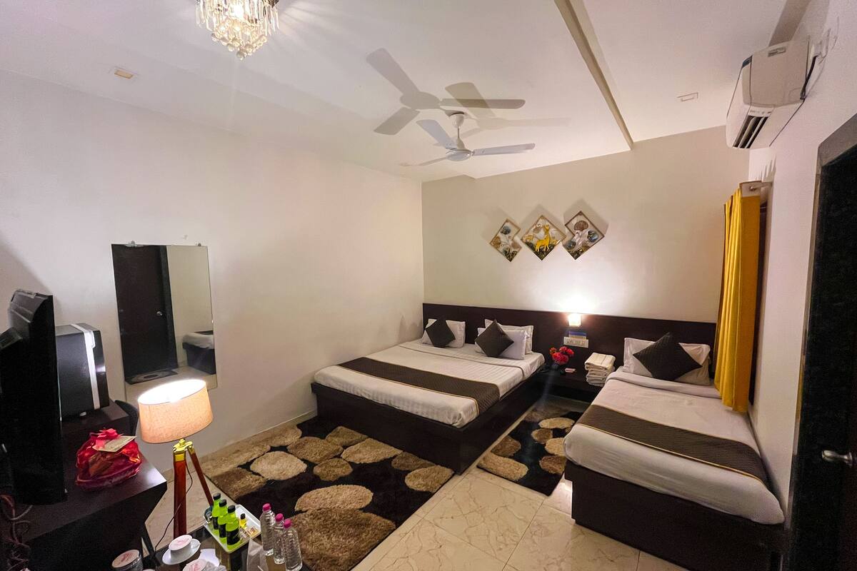 A hotel room with two beds, a desk with a lamp, a TV, a ceiling fan, and an air conditioner.