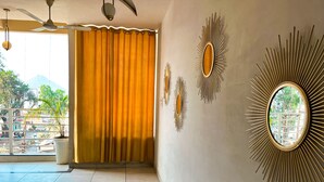 A hotel room with a large window, curtains, a ceiling fan, and decorative wall mirrors.