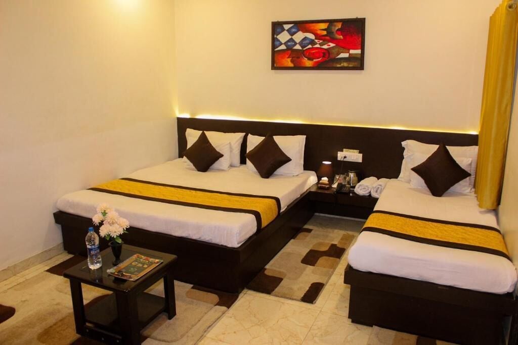 A hotel room with two beds, a nightstand, a table with a water bottle and a magazine, and a painting on the wall.