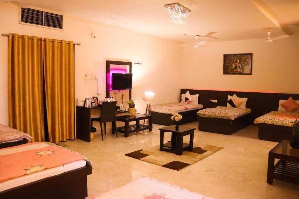 A hotel room with two beds, a desk, a chair, a small table, a ceiling fan, and a wall-mounted TV.