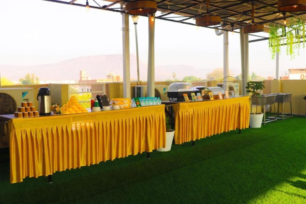 An outdoor event space with a long table covered in yellow, surrounded by greenery and a view of distant hills.