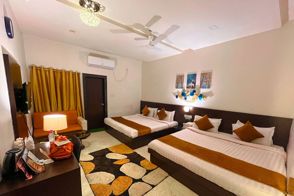 A hotel room with two beds, a desk, a chair, a TV, and a ceiling fan.