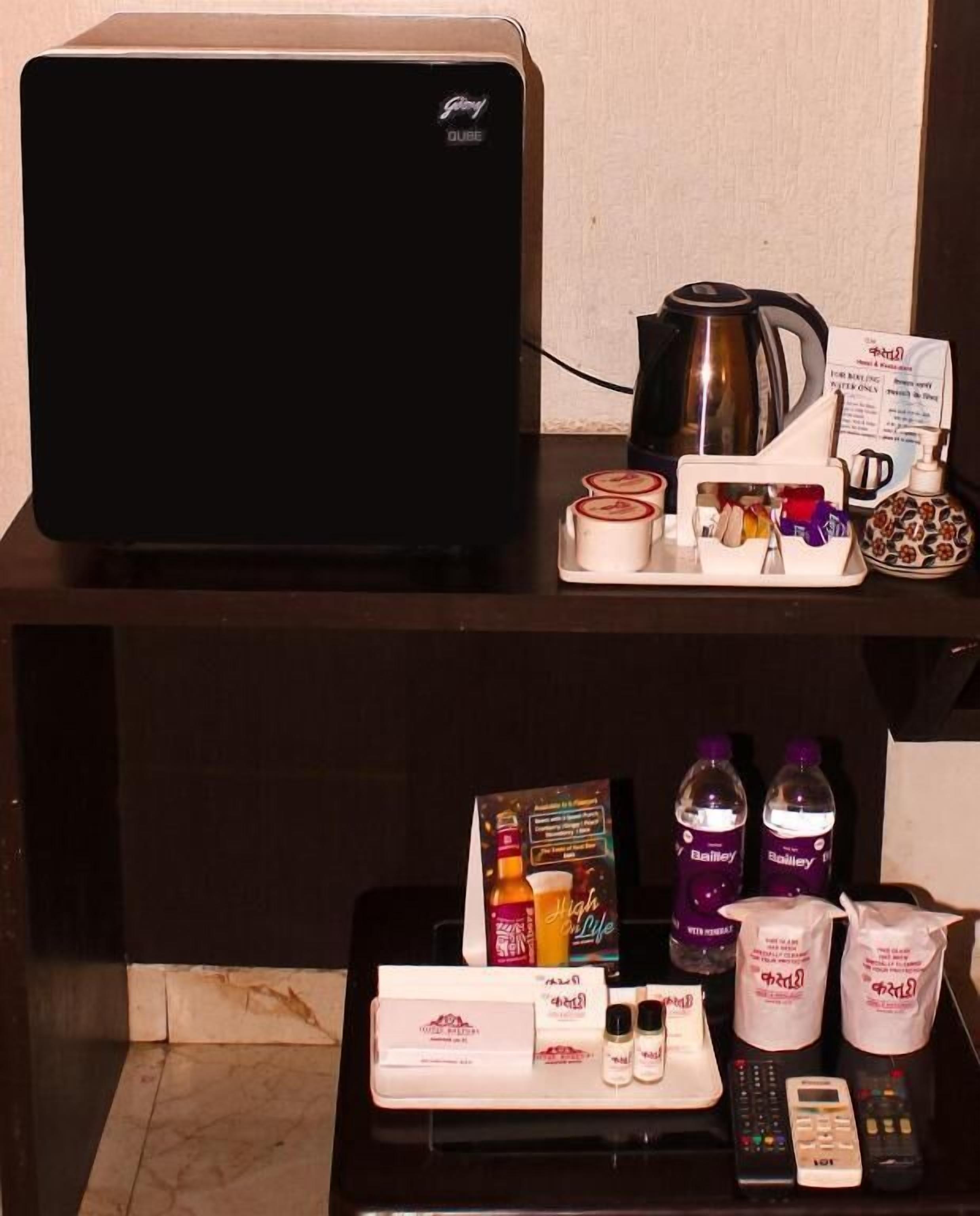 Een hotelkamer met een flatscreen televisie, een koffiezetapparaat, een dienblad met toiletartikelen en een minibar.