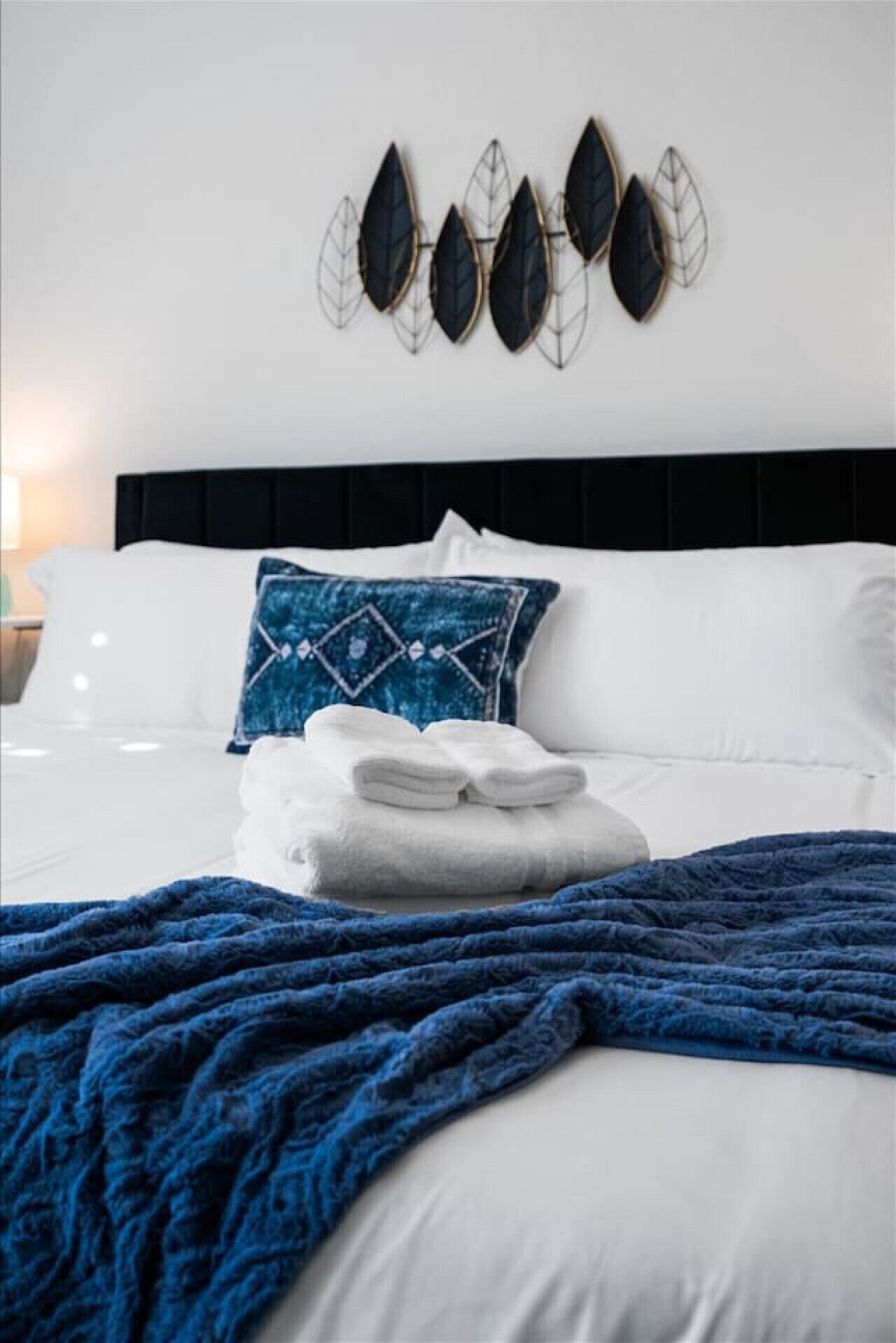 Un lit bien fait, avec des draps blancs, une couverture bleue et un coussin décoratif.