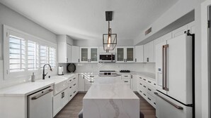 A modern kitchen with white cabinetry, a marble island, and a central light fixture. - 6th Tee Luxury | Pool & Fire Pit (Chandler)