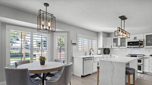 A modern kitchen with a central island, pendant lights, and a dining area with chairs. - 6th Tee Luxury | Pool & Fire Pit (Chandler)