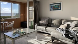 A modern living room with a leather sofa, a glass coffee table, and a view of the sea through large windows. - Waterfront fabulous view, spacious studio, heated pool & 10 mins walk into town. (Whitianga)