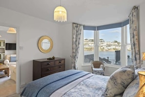 A bedroom with a bed, a dresser, a mirror, and a view of the sea.