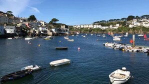 A coastal town with boats docked along the harbor, surrounded by white buildings and hills in the background. - Apartment, Sea Views & Terrace on Waters Edge (Fowey)