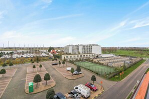 Een ruime parkeerplaats met meerdere voertuigen, een sportveld en een gebouw met balkons.