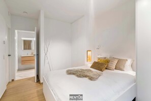 Een moderne slaapkamer met een groot bed, een nachtkastje, een spiegel en een kledingkast.