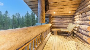 A log cabin with a wooden deck, a wicker chair, and a view of a forest. - Menninkäisenkolo by Interhome (Äkäslompolo)