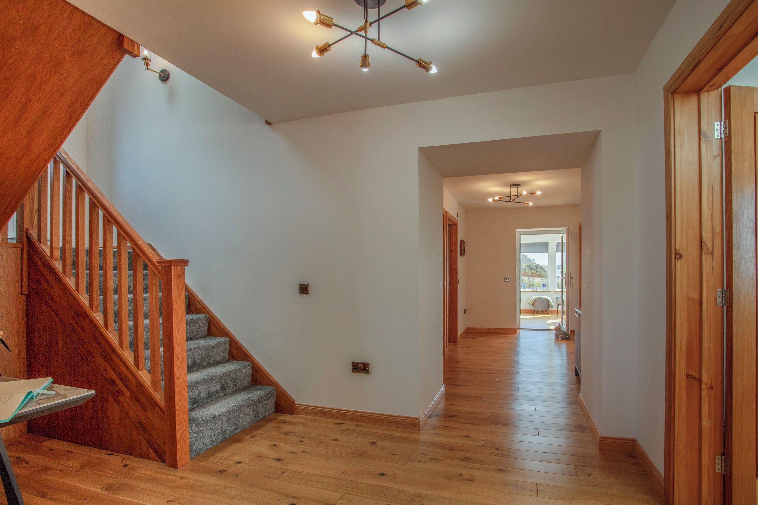 A spacious hallway with wooden flooring, a wooden staircase, and a ceiling light fixture.
