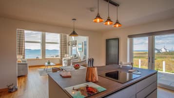 A modern kitchen with a large island, a dining area with a view, and a living room with a sofa and a table.