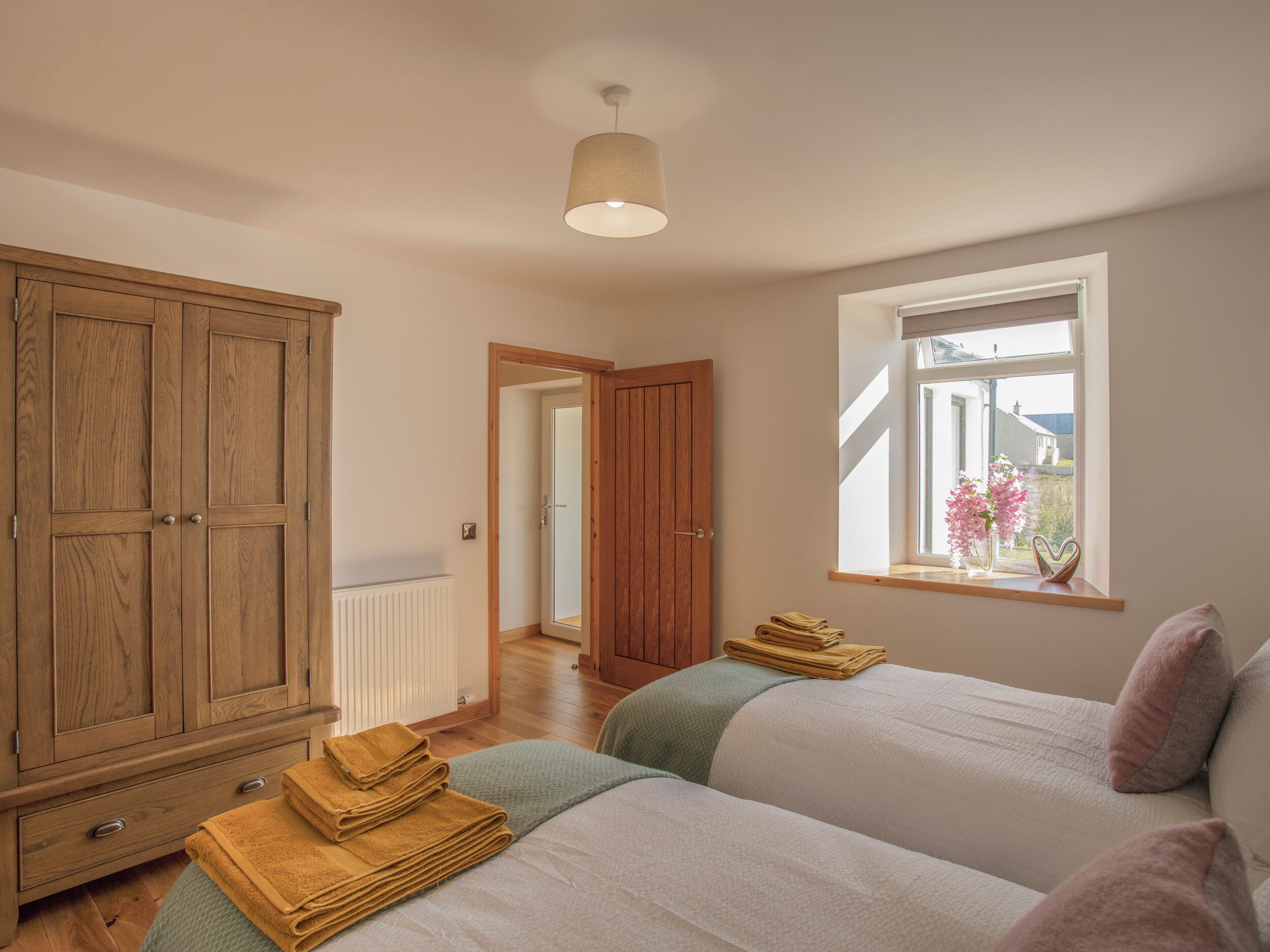 Une chambre avec deux lits, une armoire en bois, un radiateur et une fenêtre donnant sur un beau paysage.