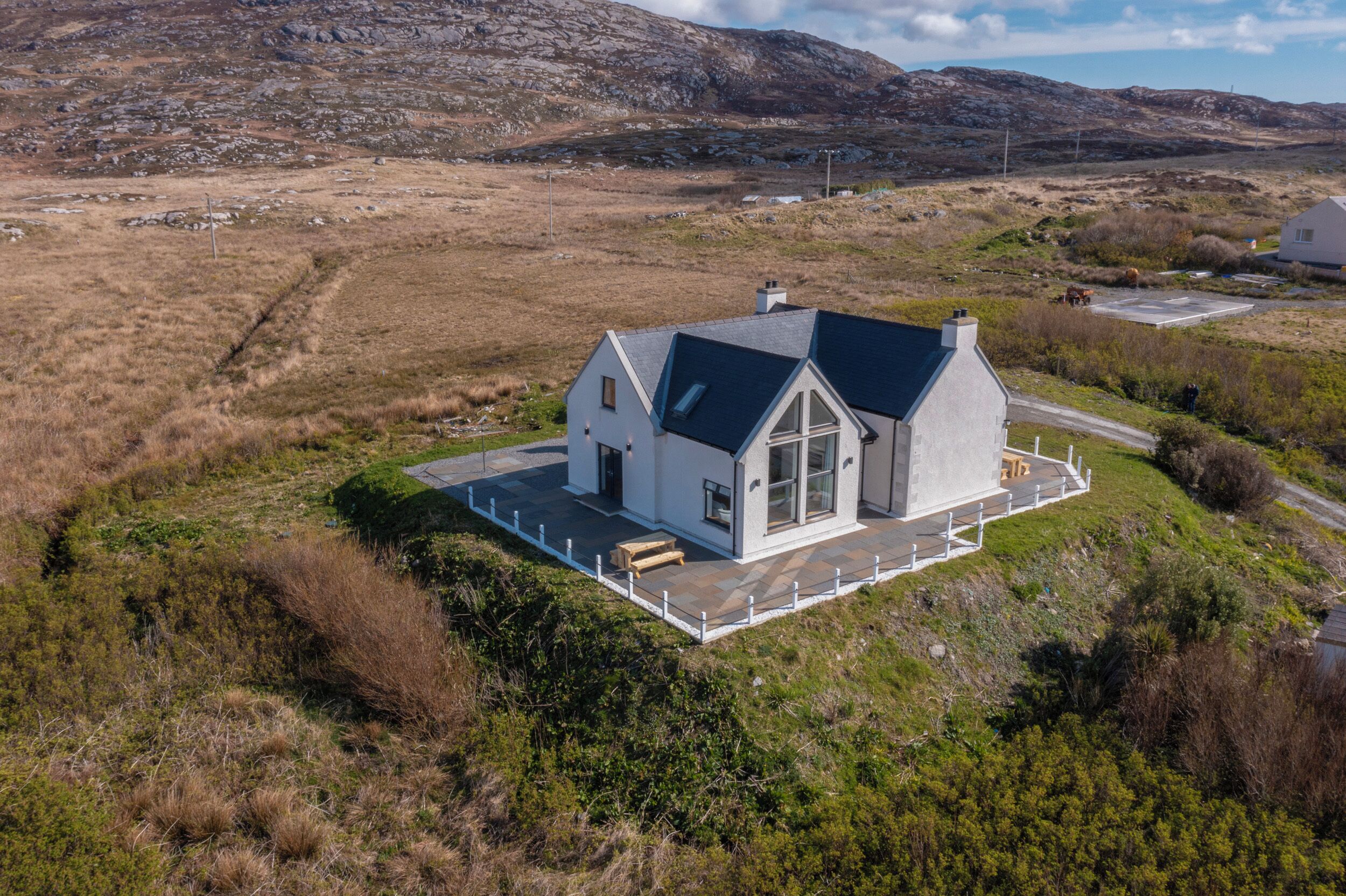 Een modern huis met een ruime veranda en een stenen fundering, gelegen in een heuvelachtig landschap.