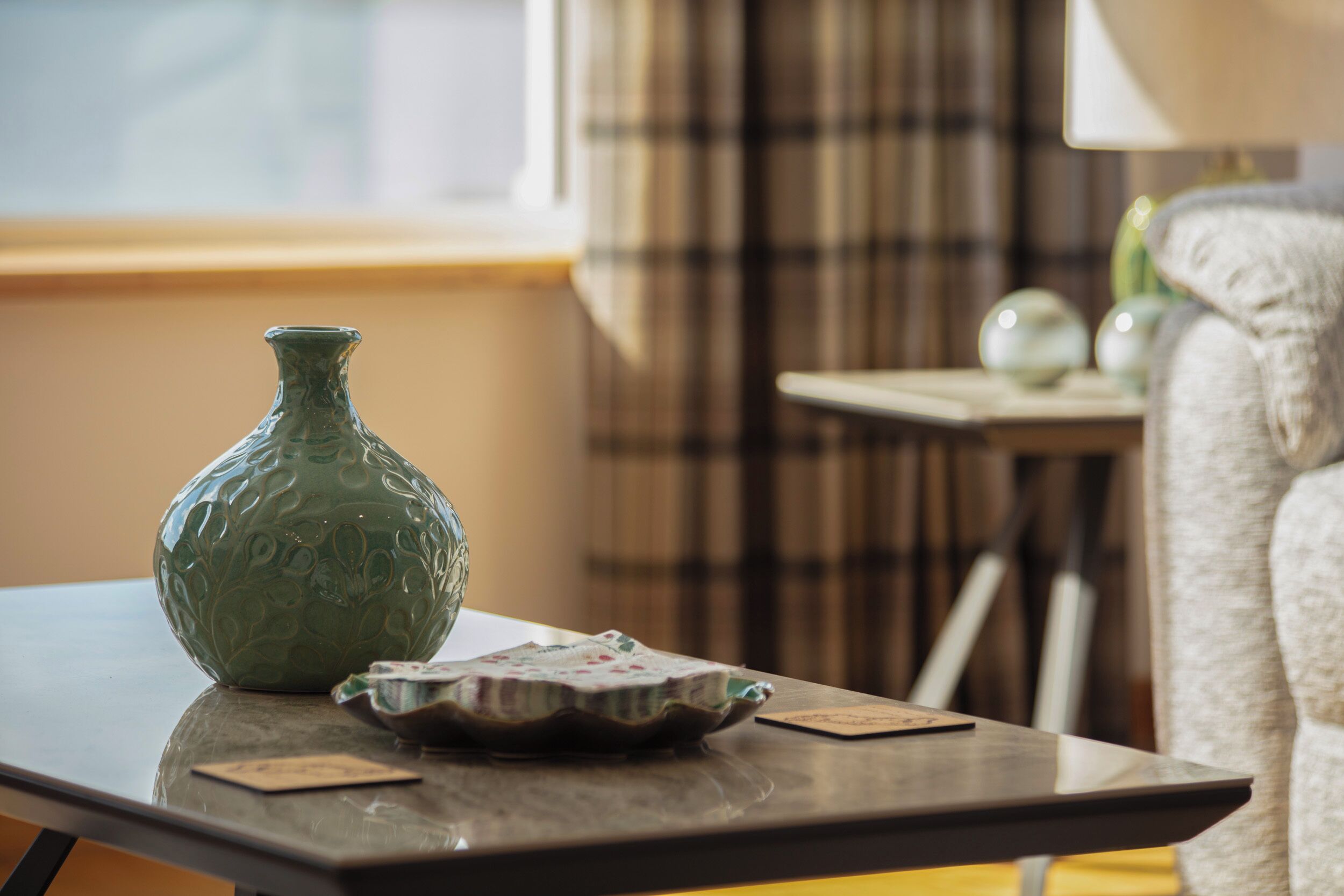 Ein Zimmer mit einem Tisch, der eine grüne Vase, einen dekorativen Teller und Spielkarten zeigt.