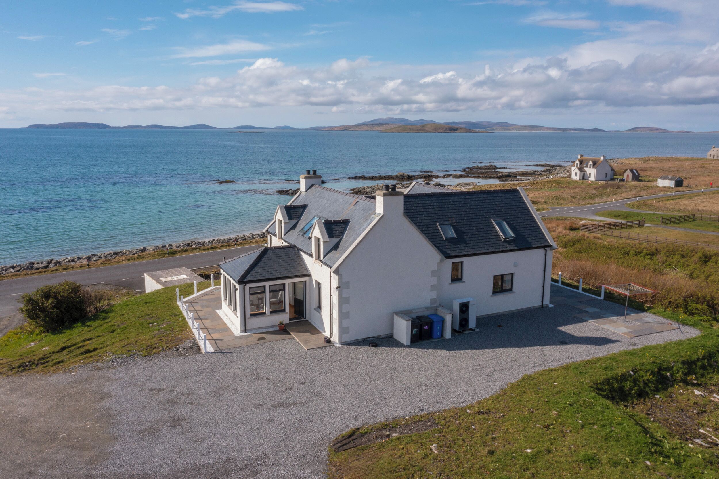 Una casa sul lungomare con vialetto sterrato, un piccolo portico e vista sul mare e colline in lontananza.