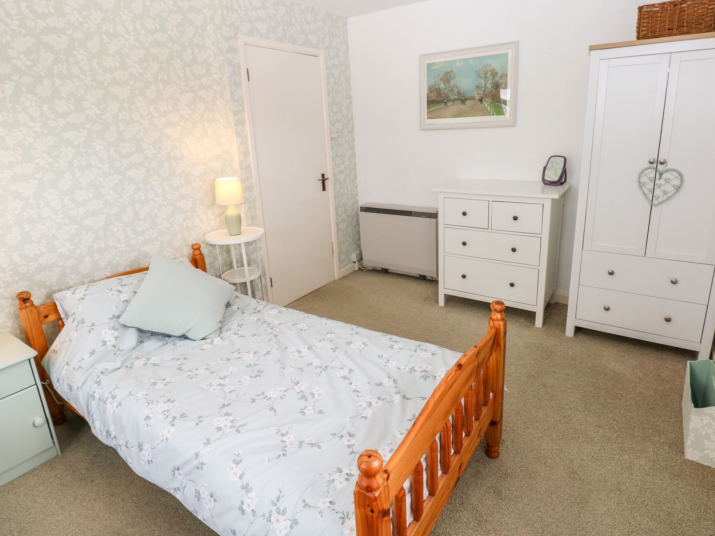 A bedroom with a wooden bed, a bedside table with a lamp, a dresser, and a wardrobe.