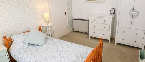 A bedroom with a wooden bed, a bedside table with a lamp, a dresser, and a wardrobe.