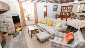 A cozy living room with a stone fireplace, a sofa set, a dining table, and a wooden cabinet. - Kenfig Farm (Pyle)