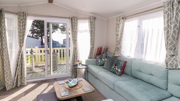 A cozy living room with a light blue sofa, a small coffee table, and a view of a deck and outdoor area. - Bay View (Bembridge)