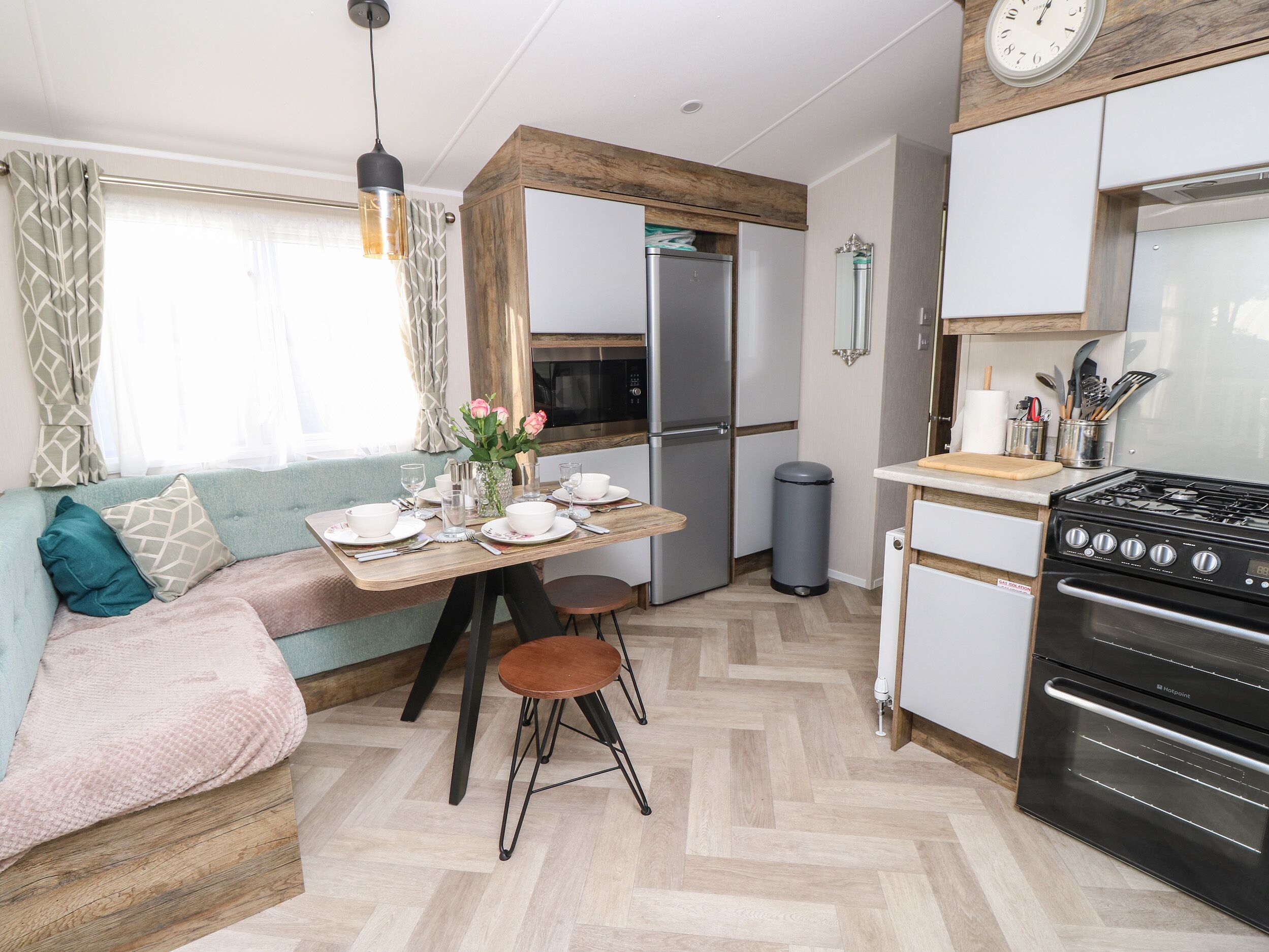 A compact kitchen with a dining area, a sofa, and a herringbone-patterned floor.
