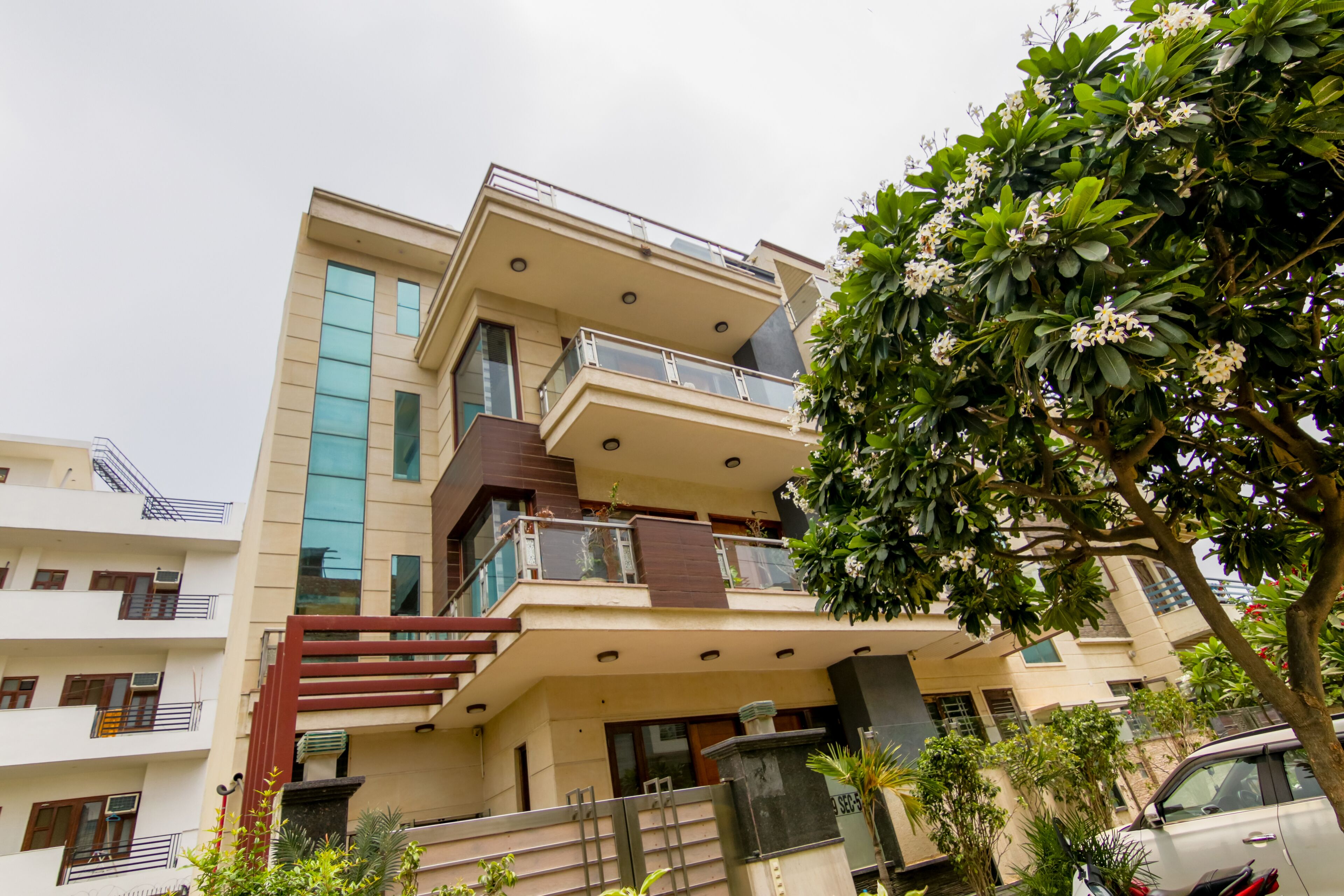 Um edifício residencial de vários andares com varandas, uma escadaria e uma árvore em primeiro plano.