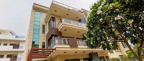 Um edifício residencial de vários andares com varandas, uma escadaria e uma árvore em primeiro plano.