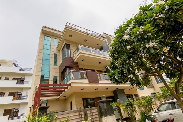 Um edifício residencial de vários andares com varandas, uma escadaria e uma árvore em primeiro plano.