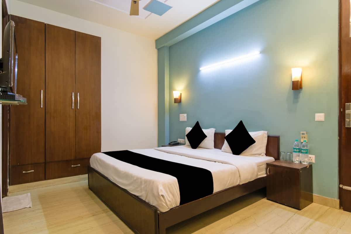 A hotel room with a large bed, wooden wardrobe, bedside tables, and wall-mounted lights.