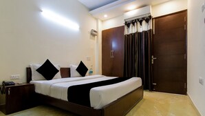 A hotel room with a large bed, a wardrobe, a bedside table, and a bathroom door. - Red Cherry (Gurugram)