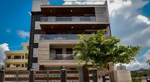 A modern hotel with multiple balconies, a tree in front, and a clear sky. - Red Cherry (Gurugram)