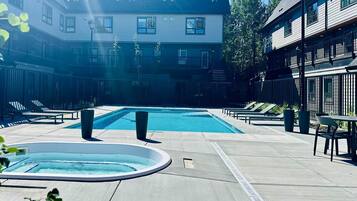 Un espace piscine avec des chaises longues, un jacuzzi et un bâtiment doté de nombreuses fenêtres.