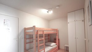 A bunk bed in a room with a white wardrobe, a small stool, and a ceiling light.