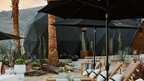 Un espace extérieur paisible, aménagé avec des chaises et des tables en osier, entouré de palmiers et dominé par un paysage montagneux.