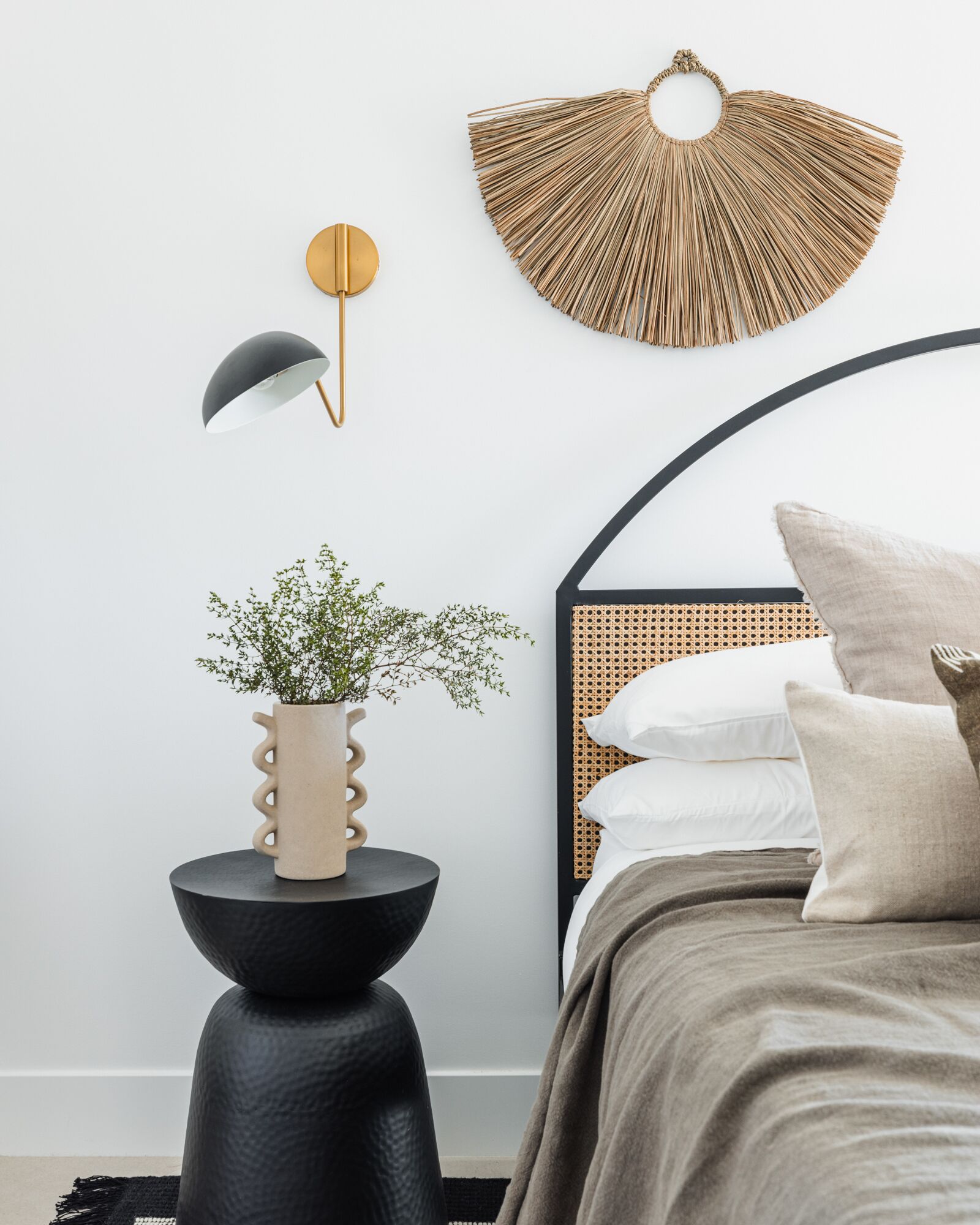 Une chambre à coucher moderne avec un lit, une applique murale ronde, un élément décoratif mural et une table d’appoint avec une plante.