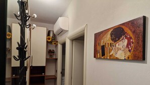 A hallway with a coat rack, an air conditioning unit, a painting, and a door leading to a laundry area.