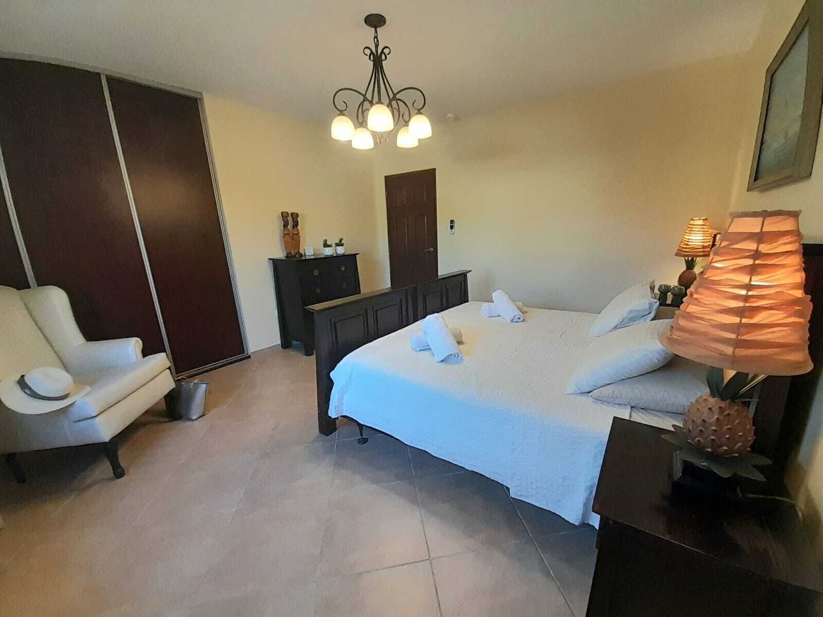Ein Hotelzimmer mit Bett, Sessel, Schminktisch, Nachttisch mit Lampe und Deckenleuchte.