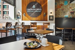 A café interior with wooden tables and chairs, a coffee machine, and a menu board.
