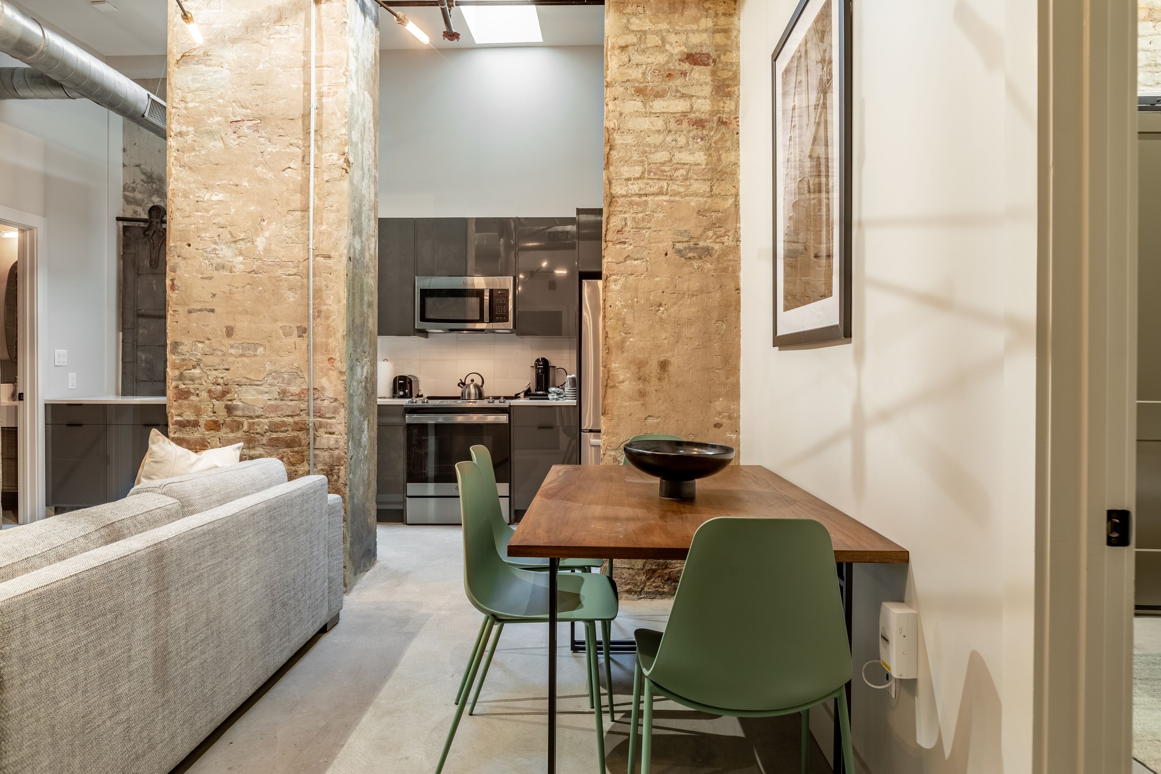 Un espacio habitable moderno con cocina, zona de comedor con mesa de madera y sillas verdes, y sofá.
